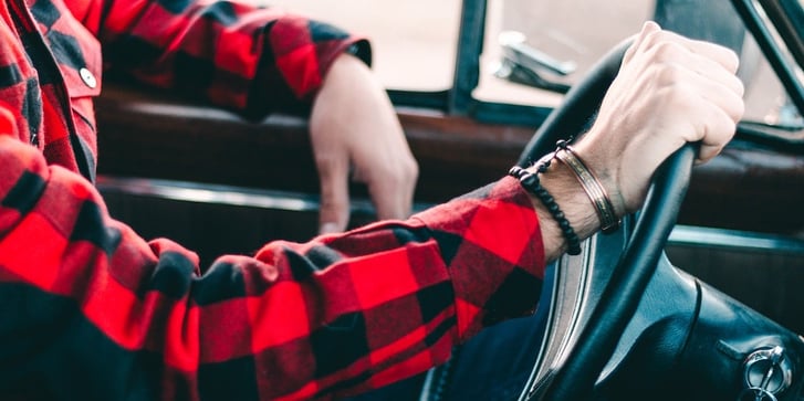 Person in plaid shirt driving car with only arms showing.