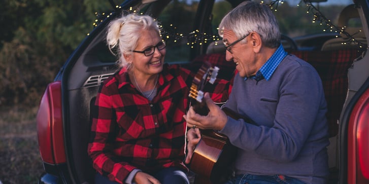 Smiling elderly couple sitting in the back seat of a car playing guitar. 